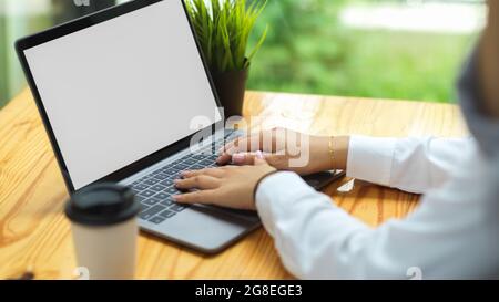 Cropped shot of businesswoman in long sleeve shirts typing on computer laptop with empty white screen at coffee shop Stock Photo