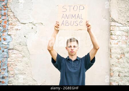 Young man holding the inscription stop animal abuse in his hands. Caucasian guy in protection of animals came out to protest. Animal rights conceptual image Stock Photo