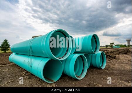 Stacked water main pipe with bell fitting next to an exposed trench for installation Stock Photo