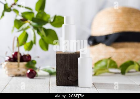 White tubes with cosmetics on a wooden podium against the background of leaves, cherry berries. Natural cosmetics.  Stock Photo
