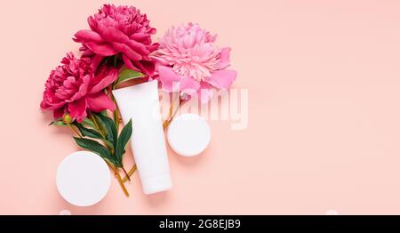 Cosmetic products cream gel shampoo balm in various bottles on a pink background with fresh flowers peonies Stock Photo