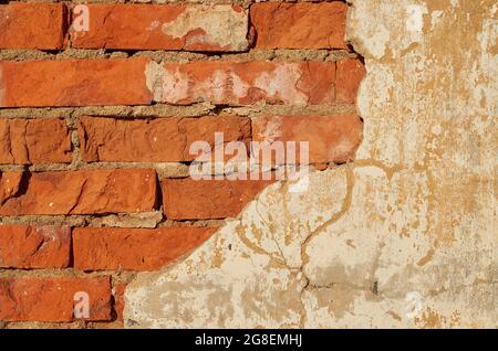 The wall is made of red brick with fallen plaster. Background.  Stock Photo