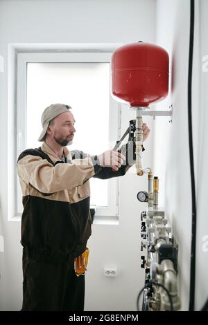 Repairman in workwear fixing part of pipe in new apartment Stock Photo