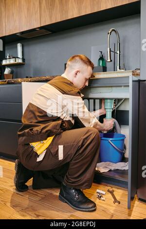 Modern plumber in workwear changing pipe under sink in the kitchen Stock Photo