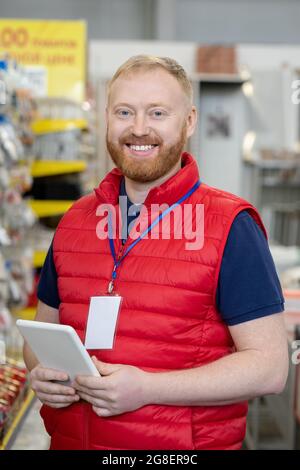 Happy bearded man in red uniform looking at you in household department Stock Photo