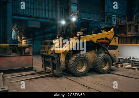 Small loading tractor or mower at work in metallurgical factory workshop. Stock Photo