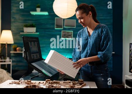 Engineer person holding maquette at layout desk for building plan and construction model concept. Caucasian woman using architectural design for measurement technology blueprint project Stock Photo
