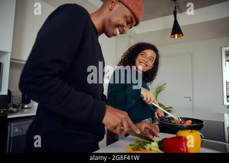 Young mixed race couple cooking food in the kitchen at home. Happy couple preparing food and smiling. High quality photo  Stock Photo