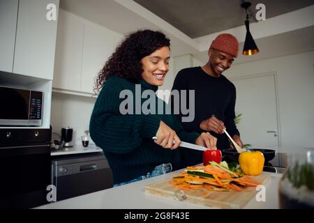 Young mixed race couple cooking food in the kitchen at home. Happy couple preparing food and smiling. High quality photo  Stock Photo