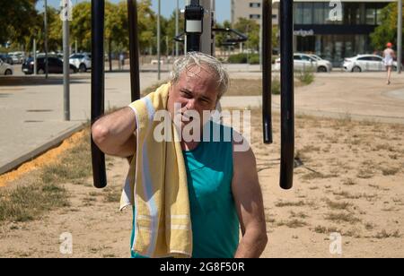 mature man wiping sweat after doing sports on the street with sports machine Stock Photo