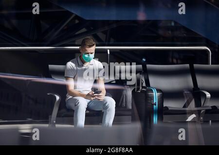 Man waiting in airport terminal and using phone. Themes mobile app, modern technology and travel in new normal. Stock Photo