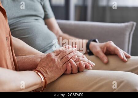 Close up of loving senior couple holding hands while sitting on couch together, copy space Stock Photo