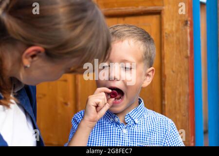 A six-year-old boy with his mother is eating fresh fragrant raspberries in the village outdoors on the porch of the house. Selective focus. Portrait Stock Photo