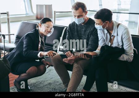Ground attendant showing flight information on phone of a couple waiting at airport. Flight attendant helping man and woman waiting for their flight d Stock Photo