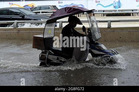 Zhengzhou, Henan, China. 20th July 2021.  A man rides on a waterlogged road in Zhengzhou, capital of central China's Henan Province, July 20, 2021. More than 144,660 residents have been affected by torrential rains in central China's Henan Province since July 16, and 10,152 have been relocated to safe places, the provincial flood control and drought relief headquarters said Tuesday. Credit: Xinhua/Alamy Live News