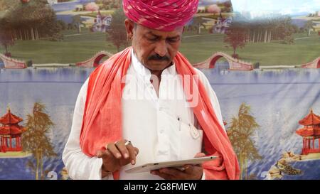Middle-aged Indian man in traditional clothing looking down at the tablet he's holding Stock Photo