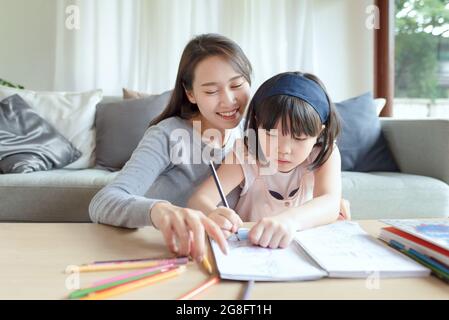 Asian mother teaching her cute kid daughter to studying in living room at home Stock Photo