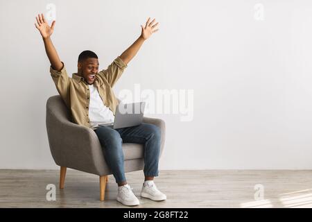 African Guy With Laptop Raising Hands In Joy, Gray Background Stock Photo