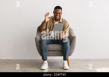 African Man Talking Video Calling Via Tablet Over Gray Wall Stock Photo