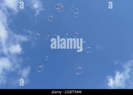 Soap bubbles floating in the air with a blue sky with clouds in the background Stock Photo