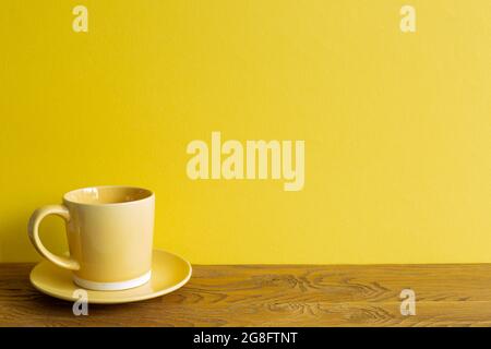 Yellow coffee cup on wooden table. yellow wall background. copy space Stock Photo