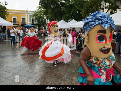 Female Cabezudos (Big Heads) dance in the De Armas Plaza after a summer rain in Old San Juan, Puerto Rico, USA. Stock Photo