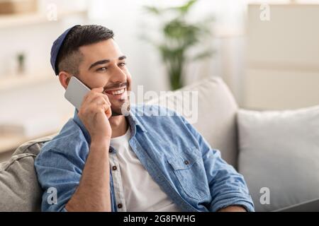 Smiling millennial man talking on phone at home Stock Photo