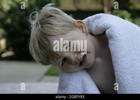 Outdoor summer garden portrait of young toddler child with blonde hair wrapped in towel Stock Photo