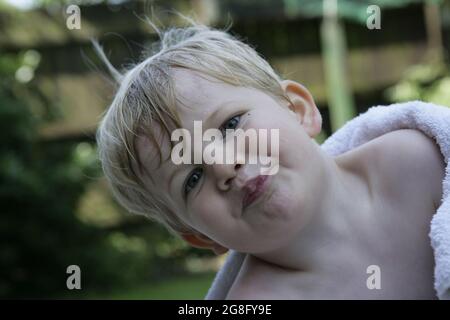 Outdoor summer garden portrait of young toddler child with blonde hair wrapped in towel Stock Photo