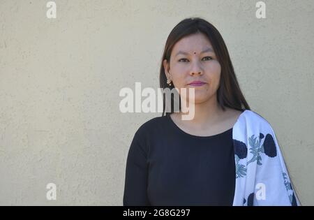 Waist up shot of a beautiful south asian young girl wearing black kurta (Indian traditional dress), standing against yellow wall with looking at camera Stock Photo