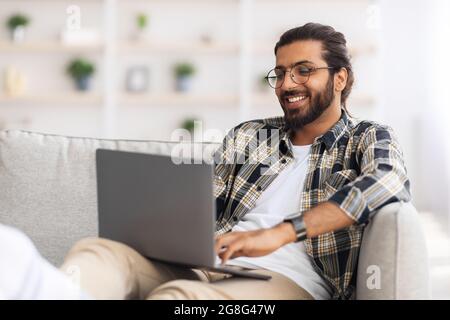 Happy indian guy working from home, using notebook Stock Photo