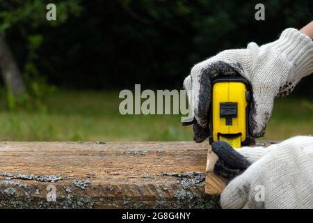 Close up of carpenter hand wearing working gloves and measuring plank with a tape measure. Stock Photo
