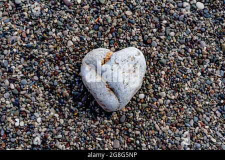 A heart-shaped stone lies on a pebble beach. Love concept. Still life. Stock Photo
