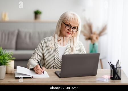Mature woman writing and using laptop at home Stock Photo
