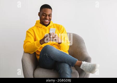 Happy Black Guy Using New Application On Smartphone, Gray Background Stock Photo
