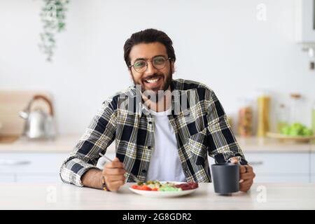 Cheerful middle-eastern young man enjoying healthy lunch at home Stock Photo