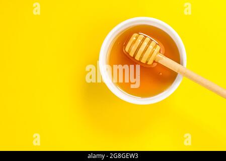 Honey in bowl with honey dipper on yellow background in top view flat lay, graphic concept, copy space Stock Photo