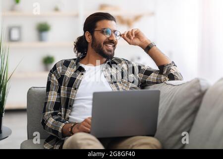 Dreamy arab guy freelancer working from home, using laptop Stock Photo