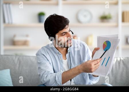 Online meeting concept. Young arab man having video call on laptop computer, showing diagram and market reports Stock Photo