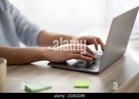 Working at laptop pc. Man typing text or programming code on computer, holding hands on laptop keyboard, closeup, crop Stock Photo