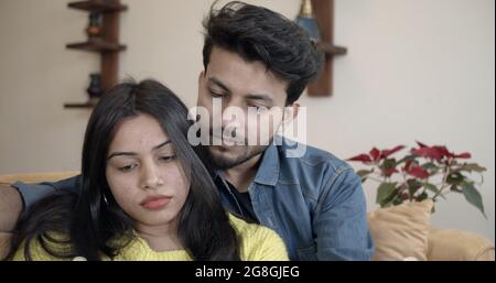 Young Indian couple sitting on the sofa and looking down on something with serious face expressions Stock Photo