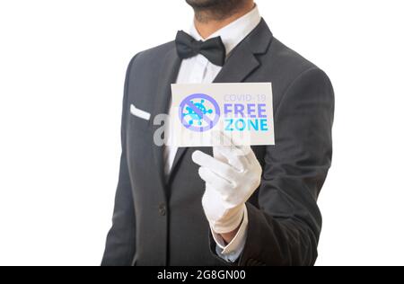 Covid free zone sign. Man waiter in suit, white background holding a card, COVID-19 free zone text . Disinfected areas, vaccinated only concept. Stock Photo