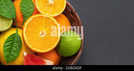 Citrus fruits in a basket on a gray stone background closeup. Citrus fruit mix. Orange, lemon and lime with leaves. Banner. Copy space, top view, flat Stock Photo