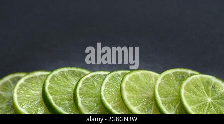 Border with sliced lime fruit closeup. Frame with green citrus on a dark stone background. Banner. Copy space. Stock Photo