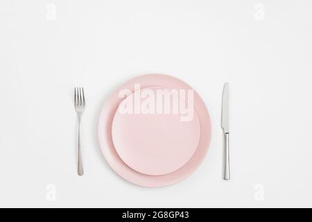 Empty pink plate and silver cutlery on a white background. Minimal table setting. Mockup or template. Copy space, top view, flat lay. Stock Photo
