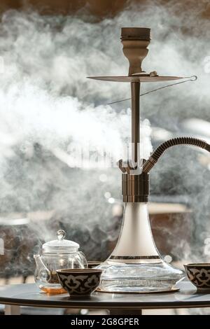 Smoking Transparent hookah on the table on the summer terrace in hookah lounge making smoke clouds and drinking tea Stock Photo