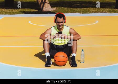 young latin man portrait playing basketball with headphones and phone in Mexico and Latin America Stock Photo
