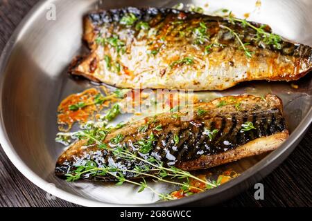 close-up of fried mackerel fillets with spices and thyme in a pan on a dark wooden table, horizontal view from above Stock Photo