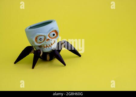 The concept of Halloween. On a yellow background, a toy skull with spider legs. Place for your text. Stock Photo