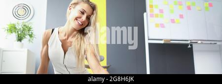 Beautiful young woman sits on the floor in the office and collects documents. Happy blonde spreads reports on the floor Stock Photo